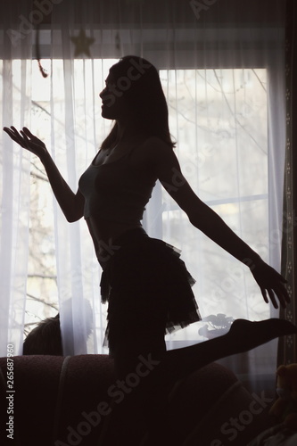 Portrait, silhouette of a sexy seductive beautiful girl dancing in a black ball gown against the bright window.