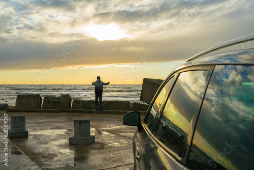Fototapeta Naklejka Na Ścianę i Meble -  Sunset on the Baltic Sea. View from the car parking. A young man admires the beauty of the sunset.