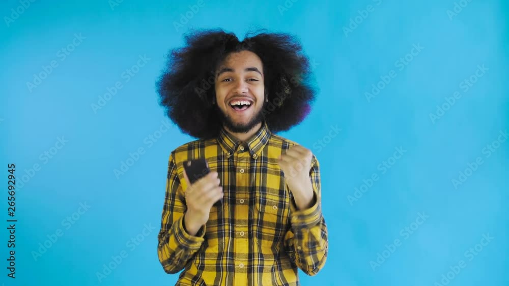 Young happy African businessman using phone and getting good news on Blue background. Concept of emotions