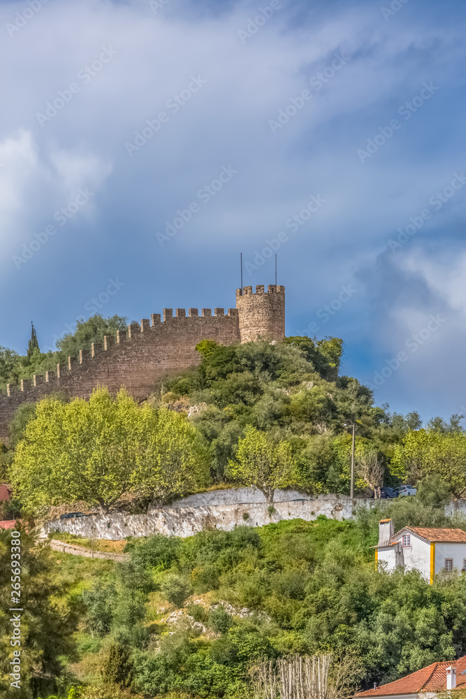 View of the fortress and Luso Roman castle of Óbidos, with buildings of Portuguese vernacular architecture and sky with clouds, in Portugal View of the fortress and Luso Roman castle of Óbidos, with buildings of Portuguese vernacular architecture and sky with clouds, in Portugal