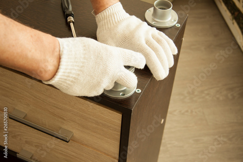 Repair and installation of furniture in the room. Male worker's hands in white gloves with screwdriver. Details and knots of furniture with bolts and fastenings. Installation of metal table legs