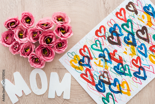top view of heart sign made of eustoma flowers, drawing and mom sign on wooden table