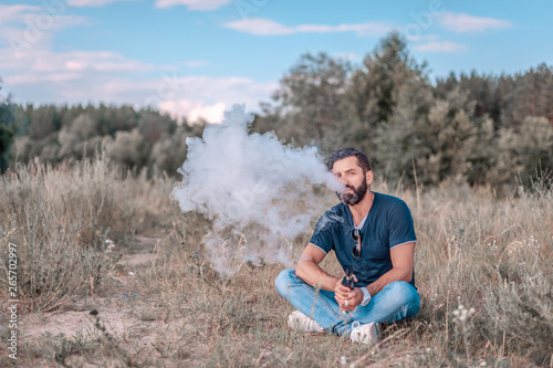 Stylish brutal vaper enjoying e-cigarette in the daylight. Hybrid cigarette.