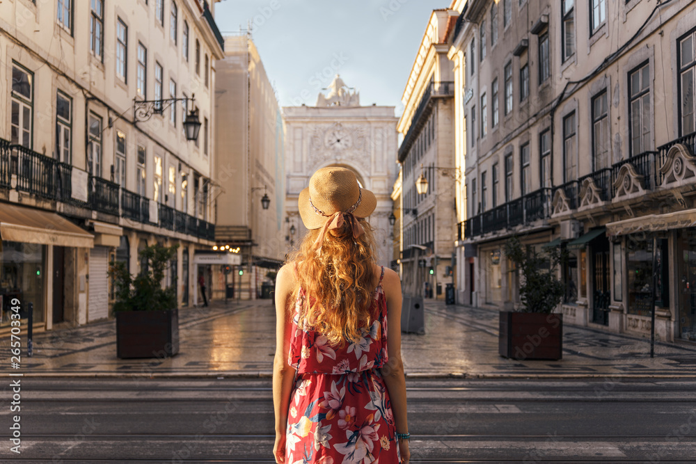 Fototapeta premium Woman in red dress and hat walking through Lisbon city centre