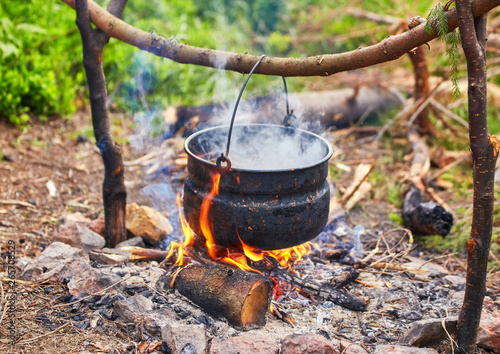 Old small kettle is heated on a bonfire on a green mountain meadow during a bad weather.