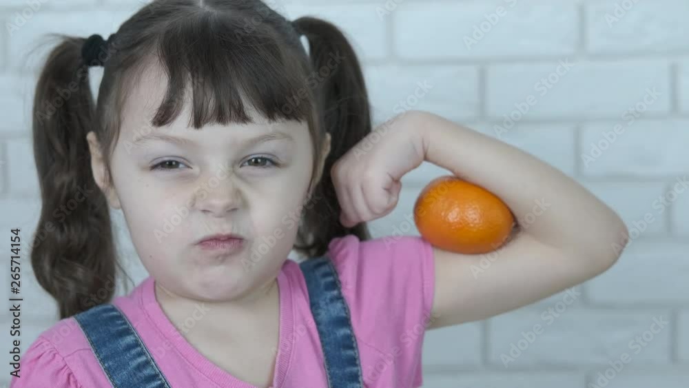 Kid shows biceps. Cheerful little girl shows mandarin biceps.
