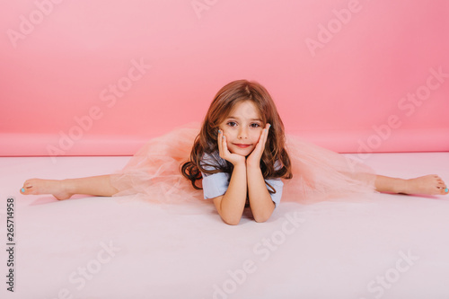 Schilderij op canvas Leisure time of joyful charming little girl making gymnastics split on floor on pink background