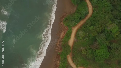 Aerial view of interesting dirt road between ocean waves and central american jungle moves bottom to top of scene photo