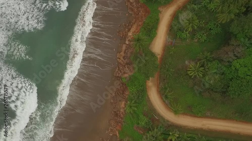 Aerial view of interesting dirt road between ocean waves and central american jungle with camera raise photo