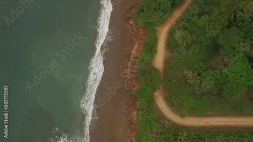 Aerial view of interesting dirt road between ocean waves and central american jungle with camera drop photo