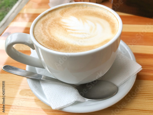 A large white cup of cappuccino with milk standing on a wooden table. Coffee mood. The concept of a break, pause. Delicious aromatic hot drink for relaxation. Close-up, yellow toning, warm atmosphere.