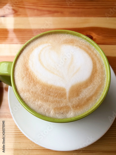 A large green cup of latte with milk standing on a wooden table. Coffee mood. The concept of a break, pause. Aromatic hot drink for relaxation. Close-up, warm atmosphere. Heart love picture