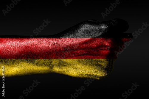 A hand with a painted Germany flag shows a fig, a sign of aggression, disagreement, a dispute on a dark background.