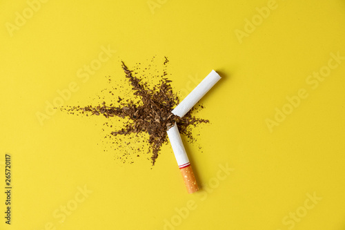 Close up cigarette broken tobacco blast spread on yellow pastel background with light side and little shadow. No and quitting smoking concept. photo