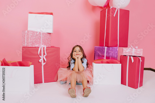 Amazing joyful little girl sitting on box suround giftboxes isolated on pink background. Lovely sweet moments of cute child celebrating birthday, expressing positivity of happy childhood to camera photo