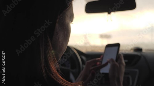 Wallpaper Mural Young woman looking to her smartphone while driving car, sun shines through front window. Girl driver use her cell phone in car. Torontodigital.ca