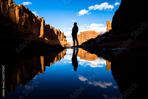 Reflection in calm lake in the desert of Southern Utah. Reflection of a man standing by the pond as well as red rock towers and canyon walls. photo