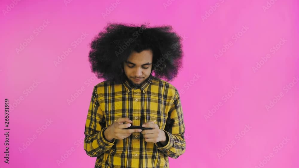 Afro-American Man Playing Game on Smartphone on purple background. Concept of emotions Afro-American Man Playing Game on Smartphone on purple background. Concept of emotions