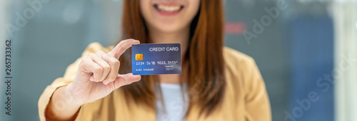 Banner of Asian woman holding and presenting the credit card for online shopping in department store over the clothes shop store, technology money wallet and online payment concept, credit card mockup