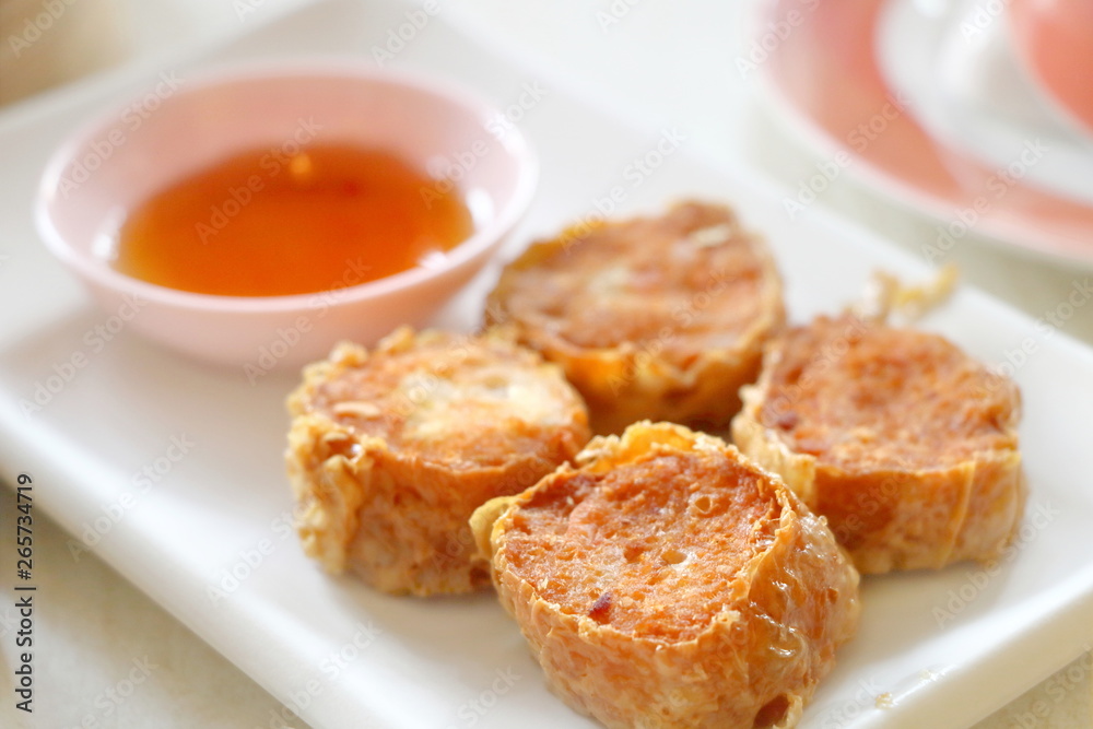 Closeup deep fried crab meat roll cake (Hoi Jo) in white plate with sweet sauce in dim sum set, crab meat in tofu wrap, Chinese restaurant food style Closeup deep fried crab meat roll cake (Hoi Jo) in white plate with sweet sauce in dim sum set, crab meat in tofu wrap, Chinese restaurant food style