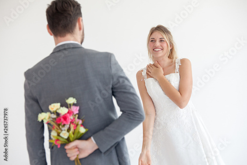 Man brings flowers to woman and hiding them behind back, Young woman looking at man with flower bouquet behind the back.