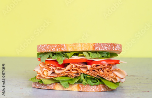 Freshly made deli style sandwich with lettus, several different kinds of vegetables, tomatoes, cheese, meats similar to ham, chicken or turkey.