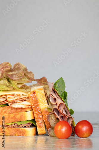 A lot of freshly sliced sandwiches on a gray background. Turkey ham on white bread with lettuce, tomatoes and cheese. Food background. photo