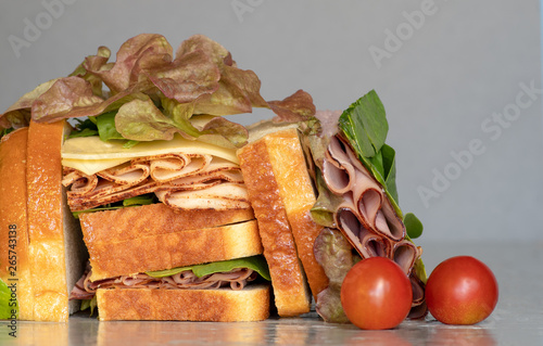 Freshly made deli style sandwich with lettus, several different kinds of vegetables, tomatoes, cheese, meats similar to ham, chicken or turkey. photo