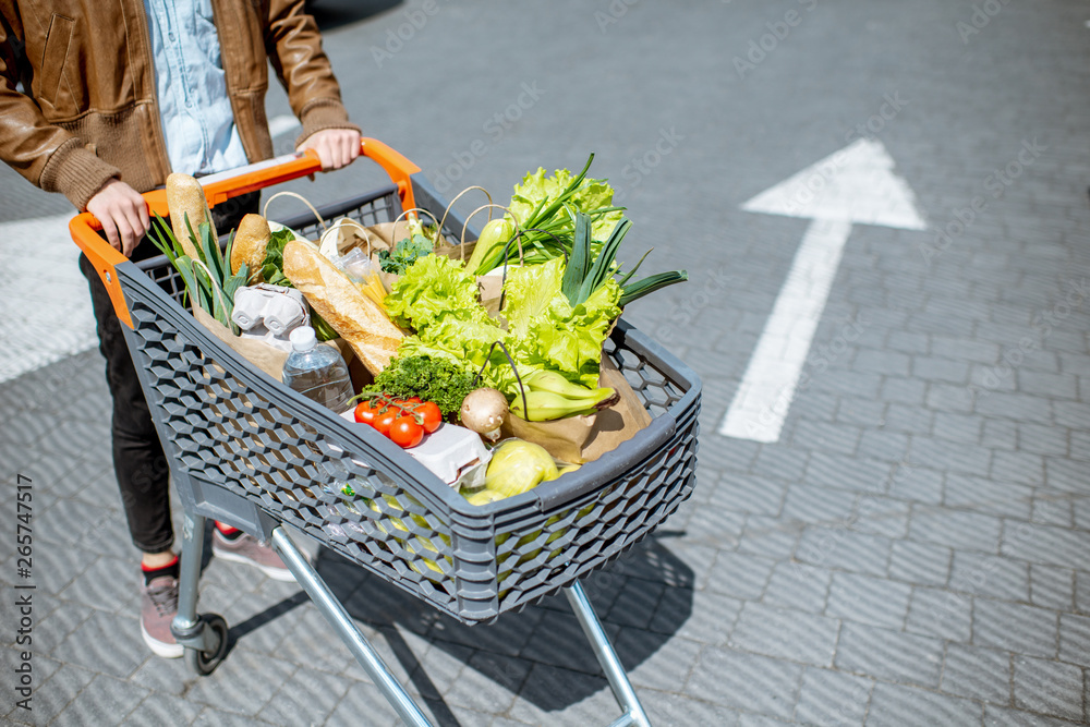 Man riding shopping cart full of fresh and healthy products outdoors, close-up view - obrazy, fototapety, plakaty 