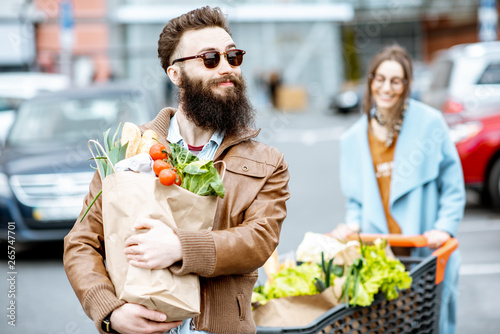 Young couple with shopping bags and cart full of fresh food on the outdooor parking near the supermarket photo