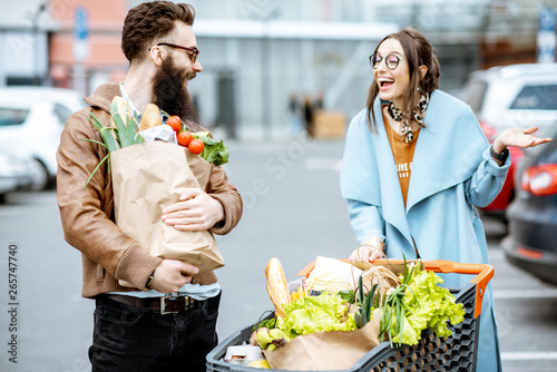 Young couple with shopping bags and cart full of fresh food on the outdooor parking near the supermarket photo