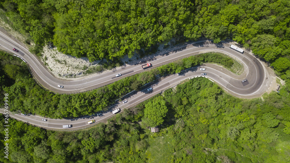 Curvy windy road in green forest, top down aerial view.
