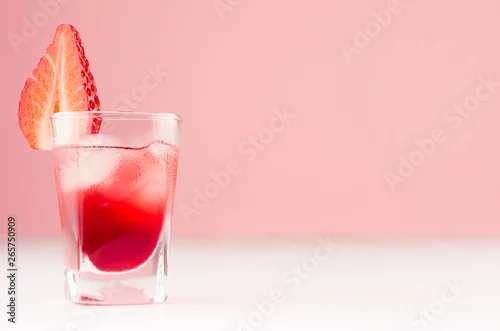 Obraz Tropikalny orzeźwienie alkohol czerwony strzał napój ozdobiony plasterek truskawki z kostkami lodu na białej desce i pastelowe różowe tło.