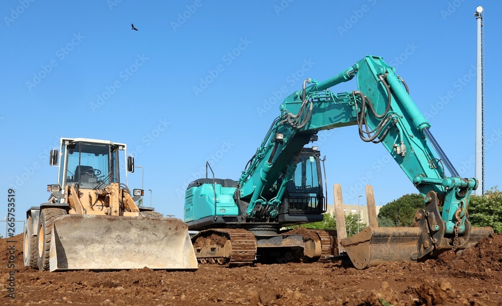 A green excavator flanked by a bulldozer on the dirt of the newly opened construction site