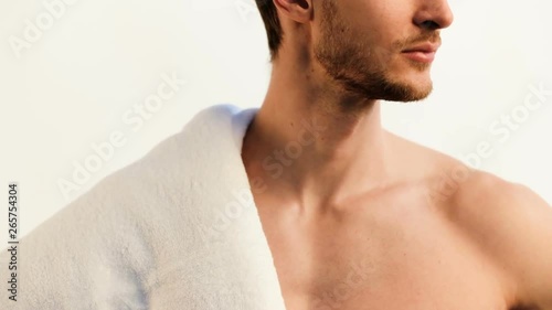 Handsome young man in mid 20s posing with white towel, showing his body, camera move from head to waste photo