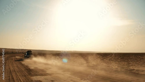 Following shot of a moving off-road 4WD silver car on desert and dust trail A big muscle 4WD offroad car driving alone on sandy way middle of wide desert and dust and sands flow under natural sunlight