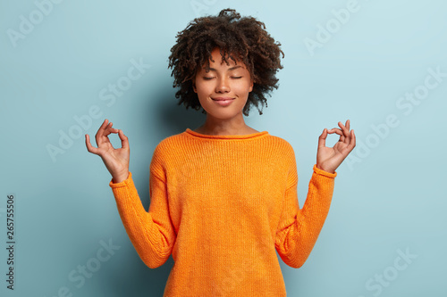 Fototapeta Mindful peaceful Afro American woman meditates indoor, keeps hands in mudra gest