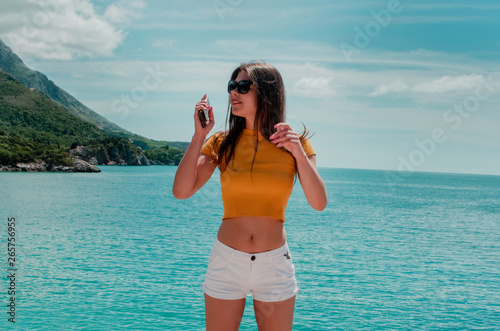 sporty young beautiful woman with a phone in her hand posing on a background of mountains and the sea