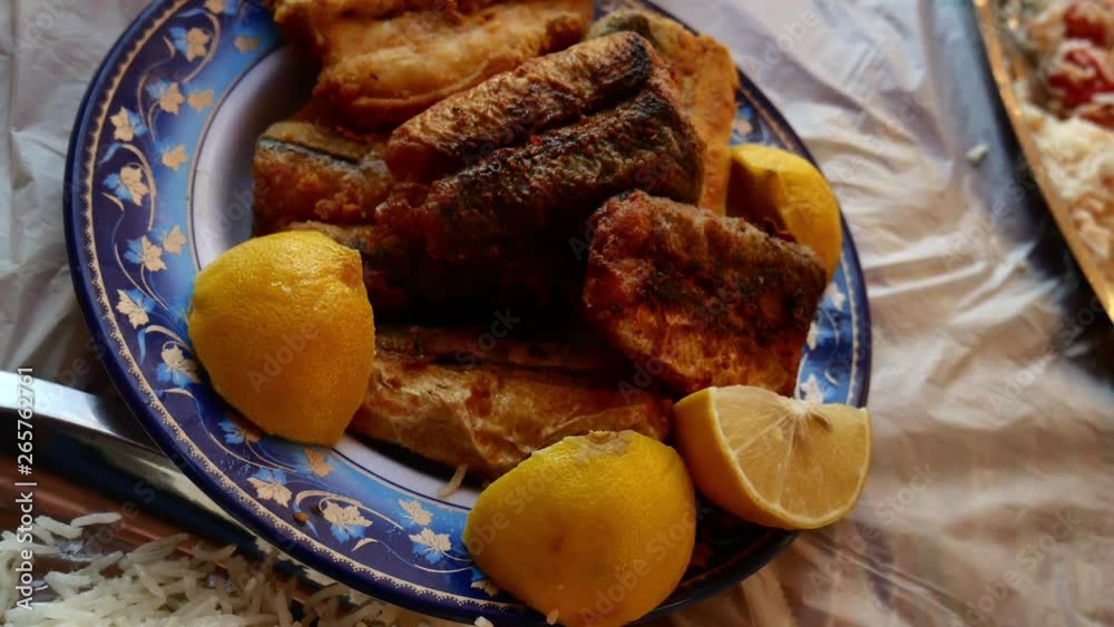 Rotating close up shot of eastern fried fish piece and fresh cut lemon A white and blue color dish full of delicious fried pieces of fish with fresh lemon cut with Persian gulf fishes