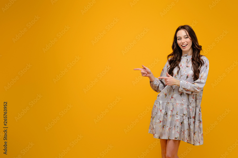 Young woman smiling pointing at copy space isolated over yellow background Young woman smiling pointing at copy space isolated over yellow background