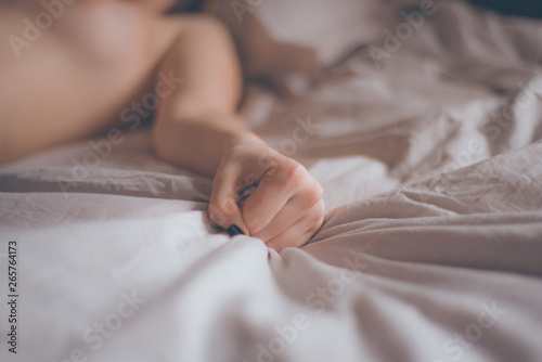 Hand sign orgasm of woman on white bed. Hand of female pulling white sheets in ecstasy. Feeling and emotion concept. Love sex concept. photo