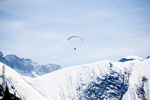 one blue parachute flying free in the sky over a snowed mountain