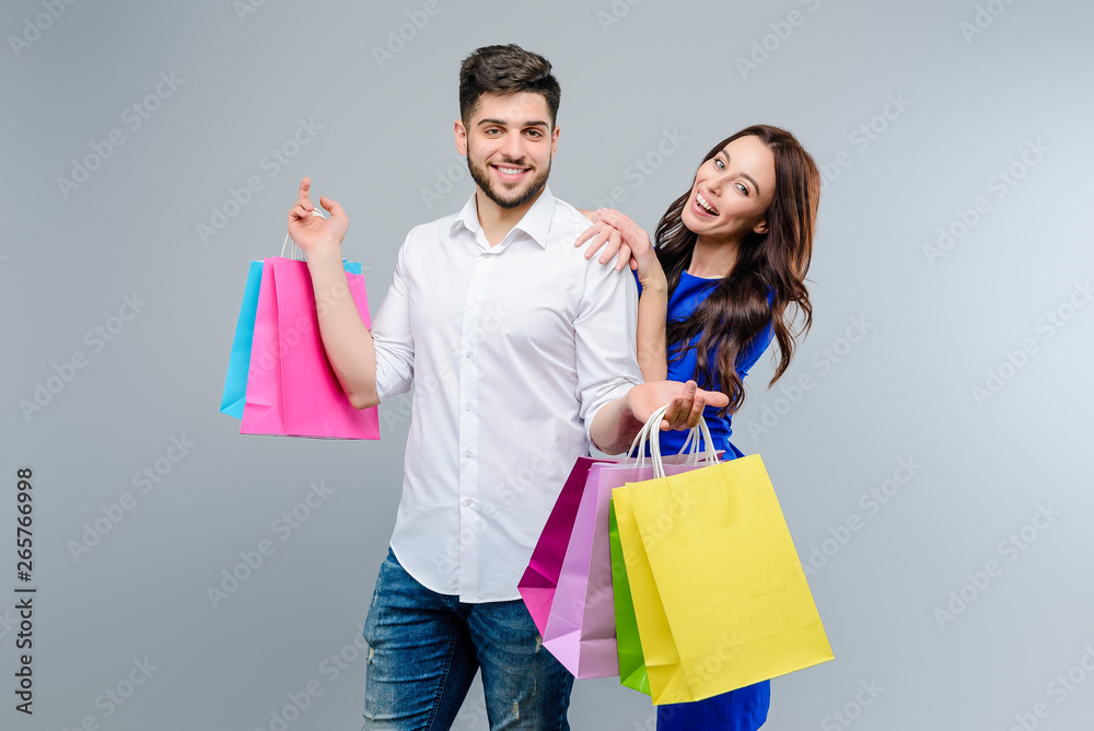 Attractive young couple with shopping bags from mall isolated over grey background. Girl shops with boyfriend on black friday sales Attractive young couple with shopping bags from mall isolated over grey background. Girl shops with boyfriend on black friday sales