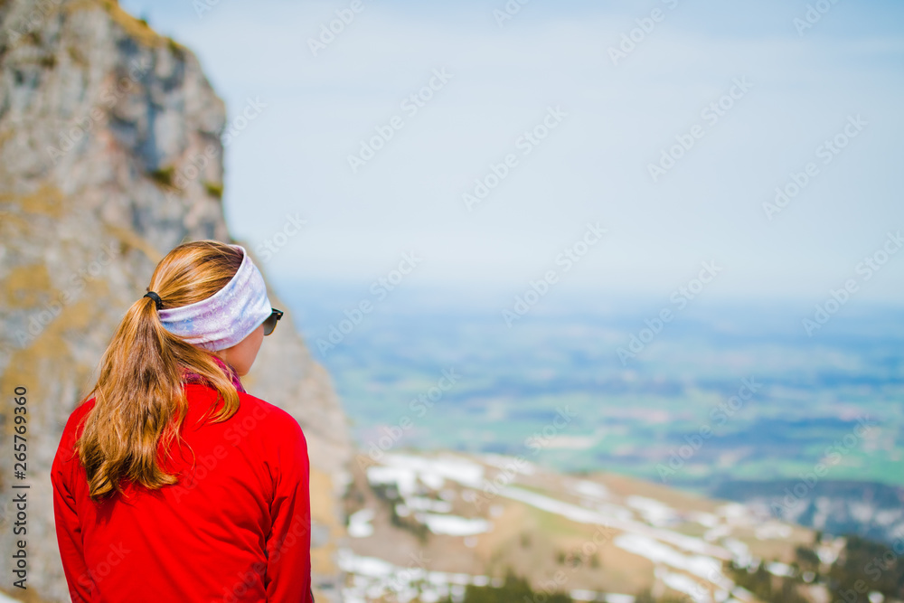 Junge Frau sitzt auf einem Berg in den Allgäuer Alpen und schaut in die Ferne des Tals