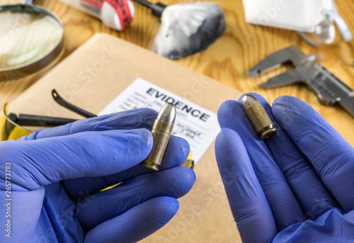 Expert police officer comparing two nine millimeters bullets in ballistics laboratory