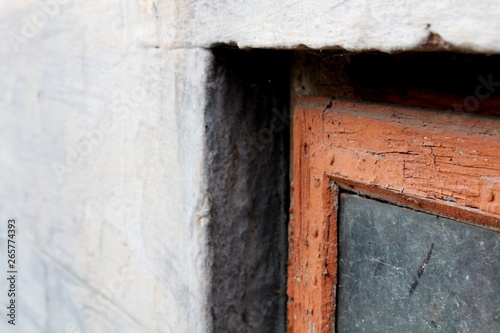 An old window in a red frame with dirty glass on a gray facade. The view is close. © Romaniia