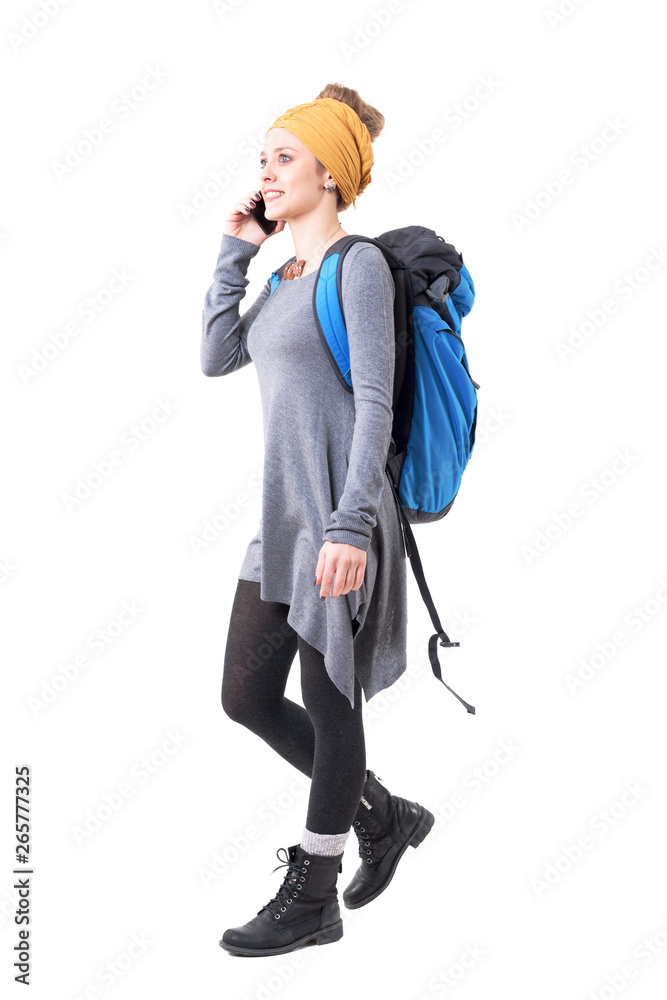Cheerful excited young traveler woman with backpack walking and talking on the mobile phone. Full body isolated on white background. Cheerful excited young traveler woman with backpack walking and talking on the mobile phone. Full body isolated on white background.