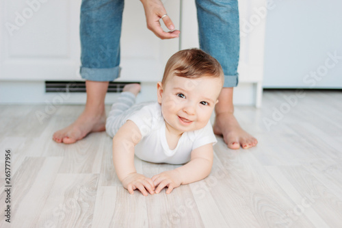 Charming little boy 6 months smiling and looking at the camera on the background of mom's feet photo