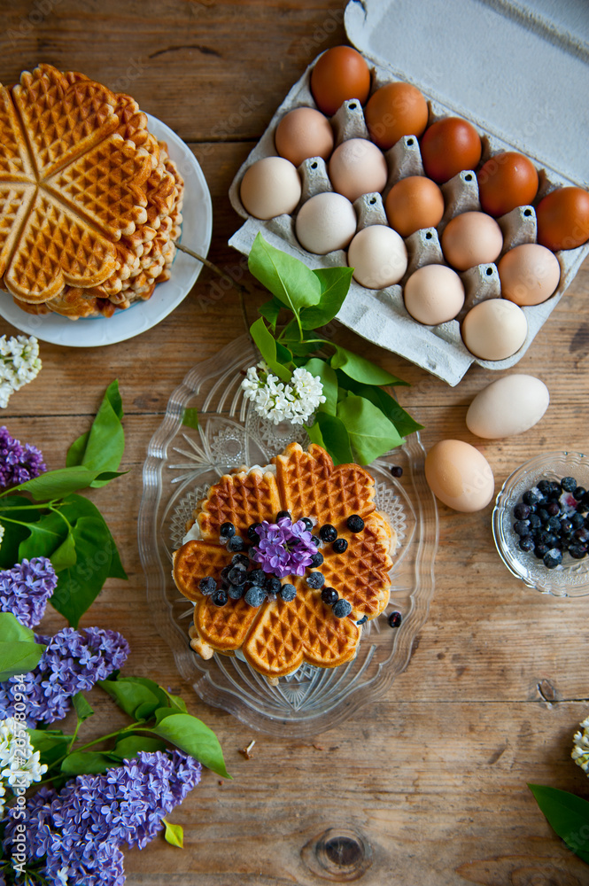 Homemade waffles with aronia, eggs and lilac flowers on the wooden table Homemade waffles with aronia, eggs and lilac flowers on the wooden table