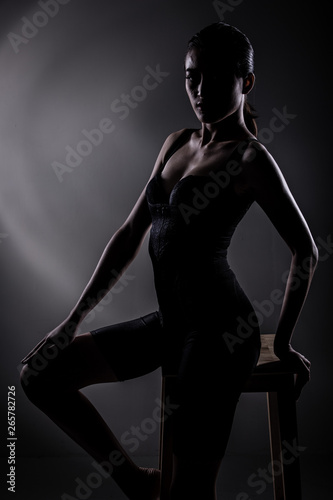 Healthy and Fit Sport Asian Woman in Bodysuit Underwear posing strong and bad feeling weight loss control, black corset body slim dress on asia girl. Studio lighting dark smoke background low exposure